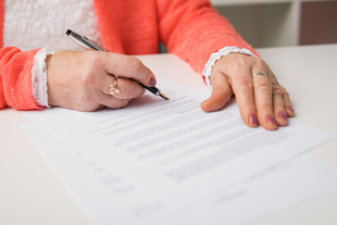 close up of an older woman’s hands signing a document