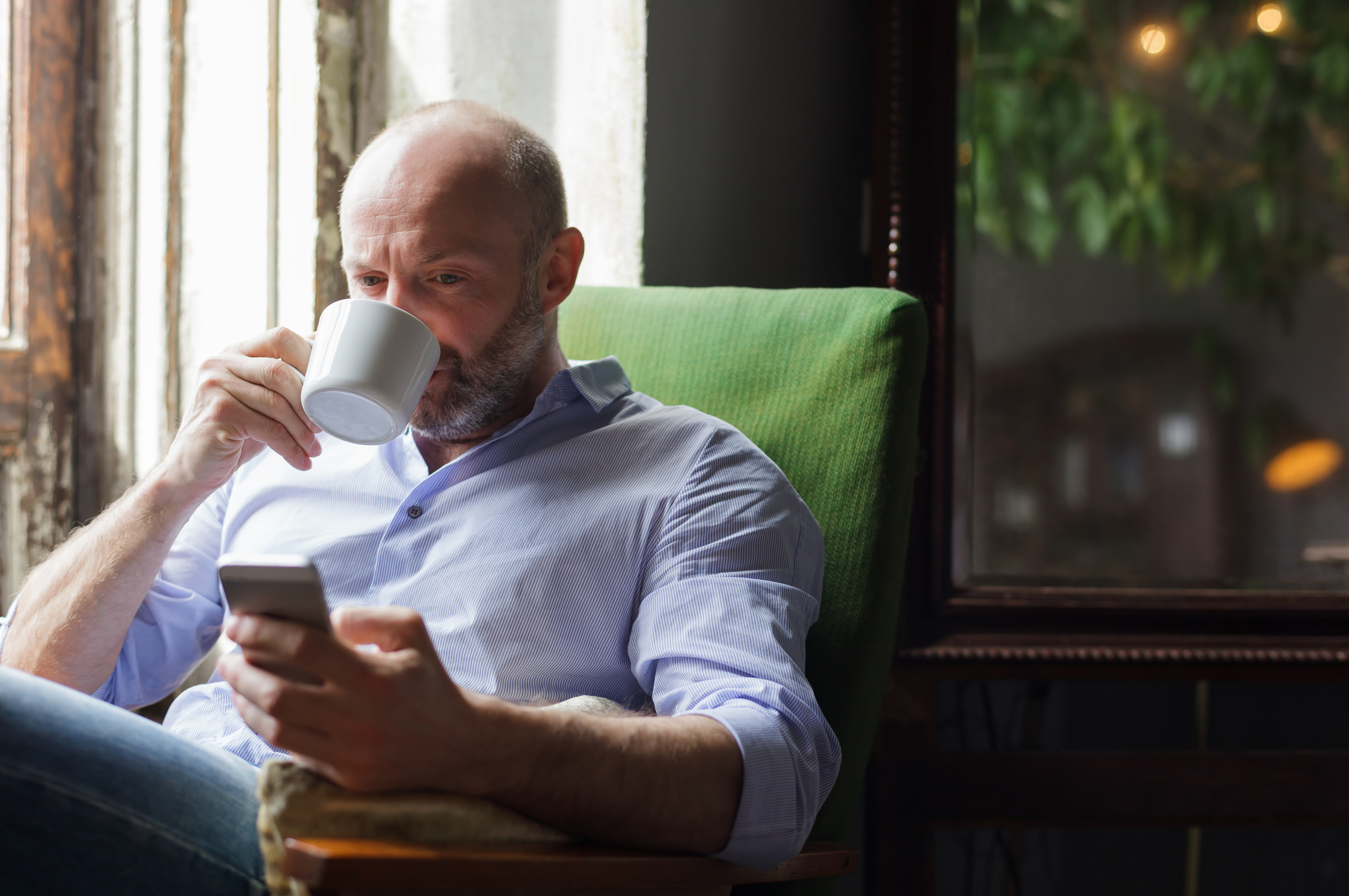 man drinking coffee while looking at phone