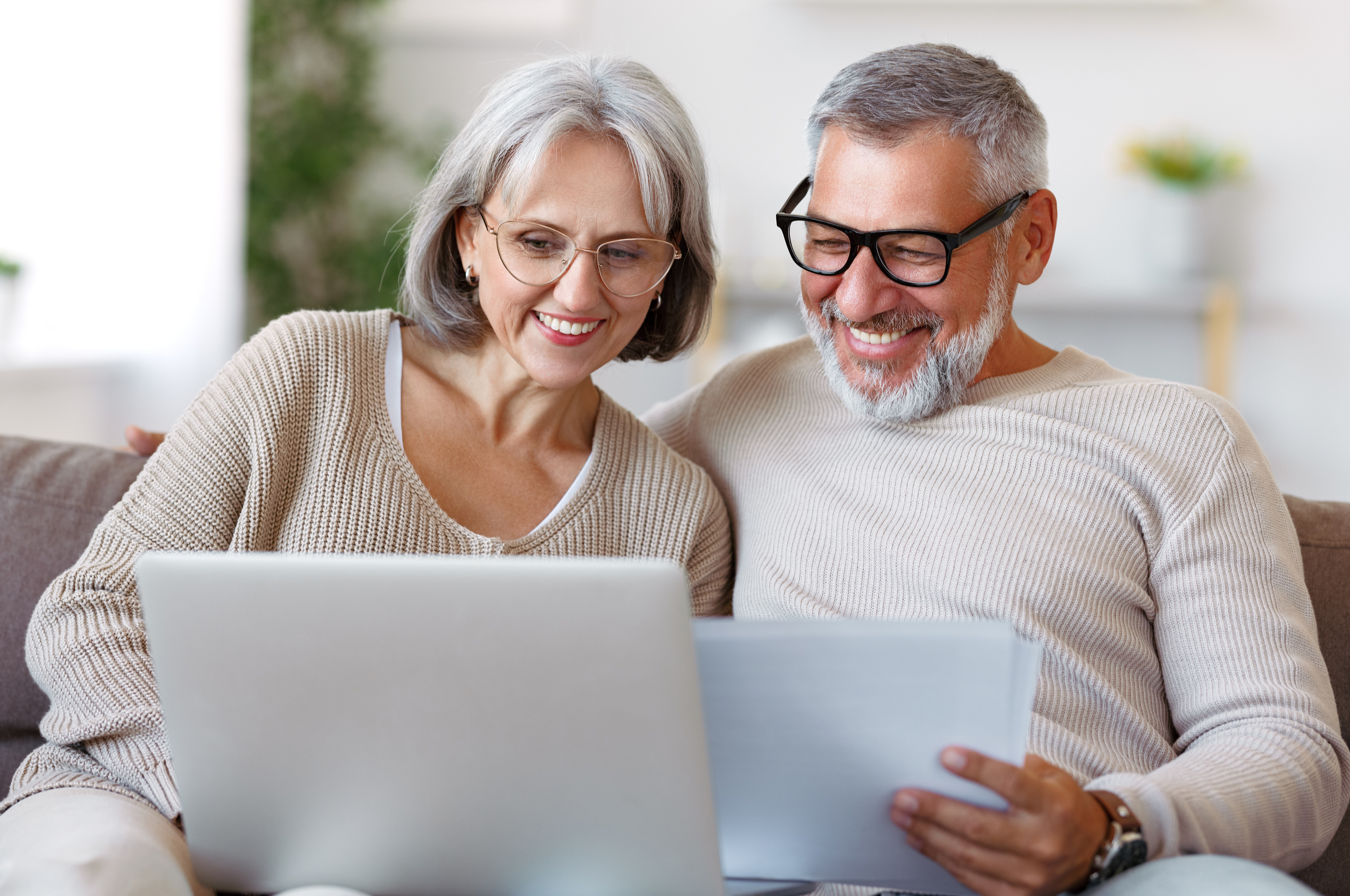 smiling middle-aged couple reading paperwork and looking at laptop
