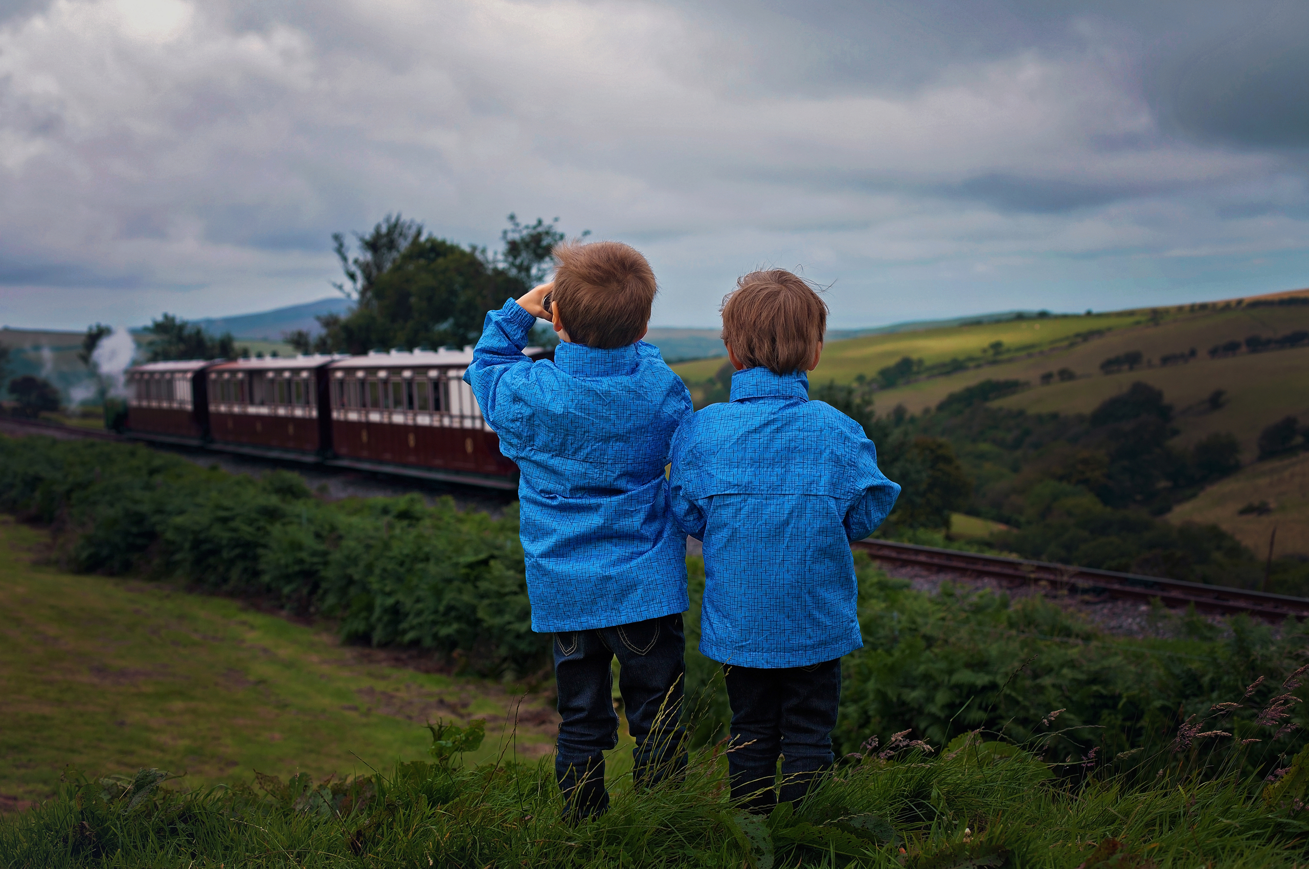 Two young boys look at a steam train on a railway