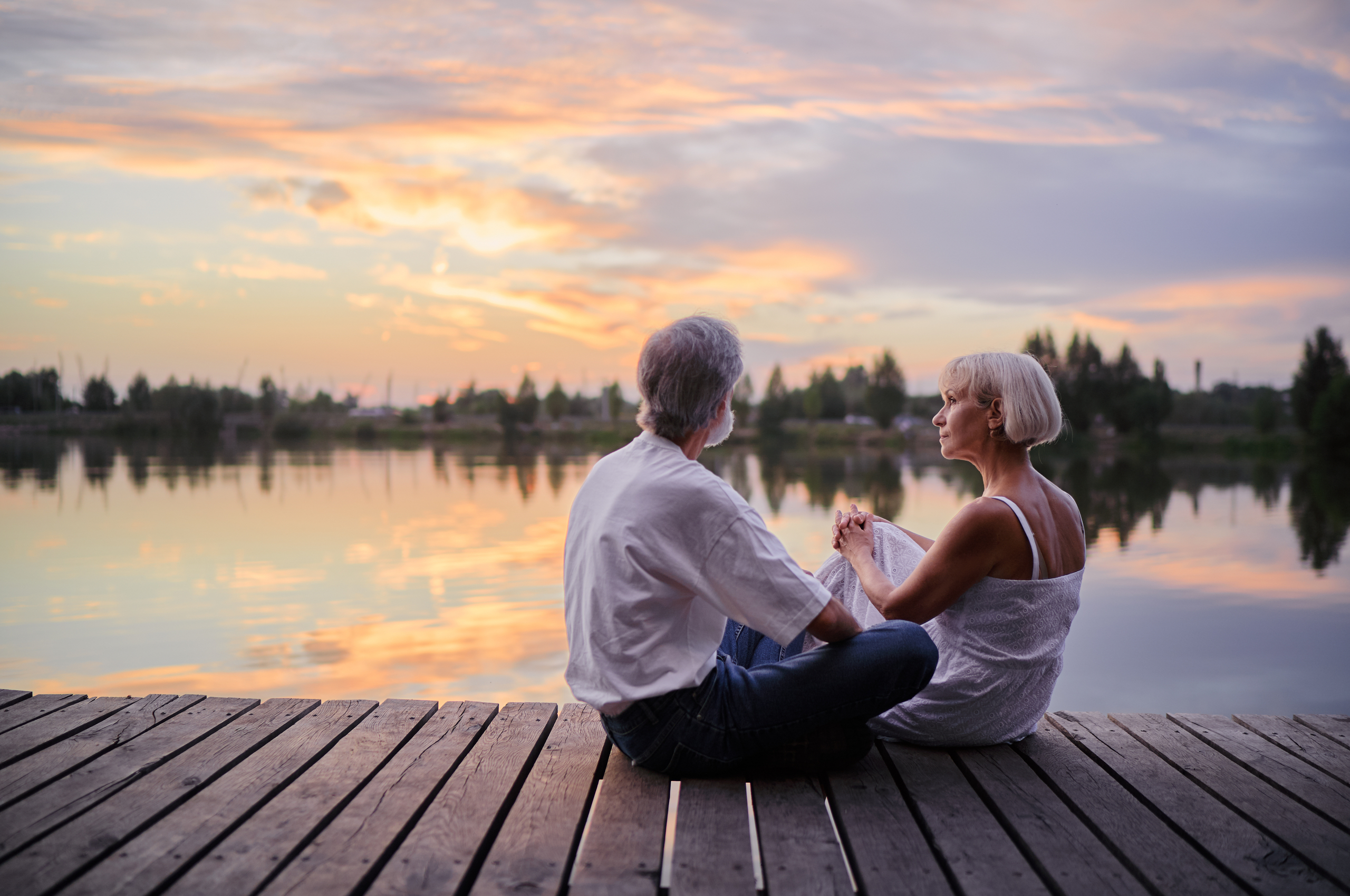 Middle-aged couple sit on a pontoon by a lake at sunset