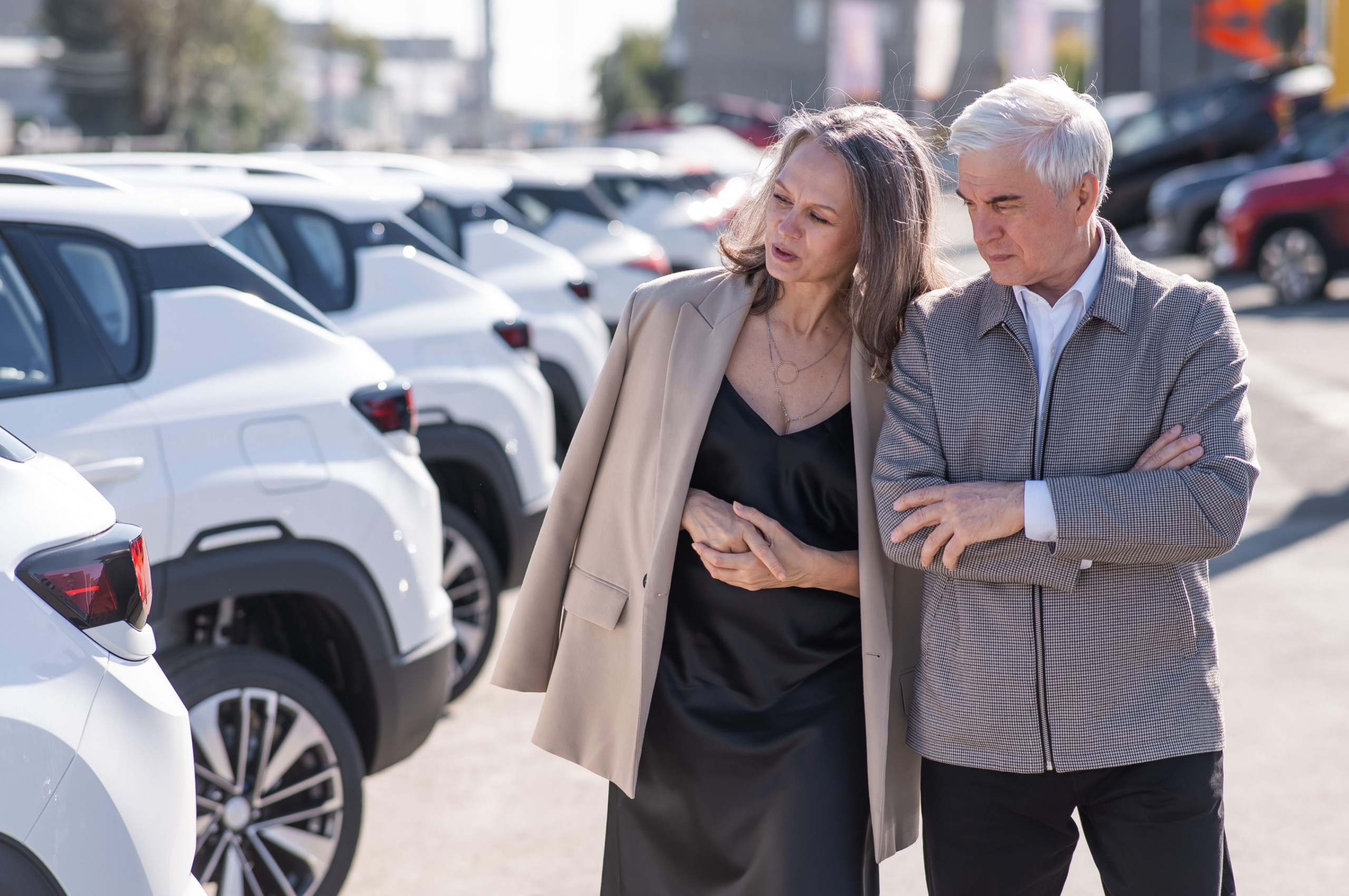 Middle-aged couple look at new cars on a forecourt