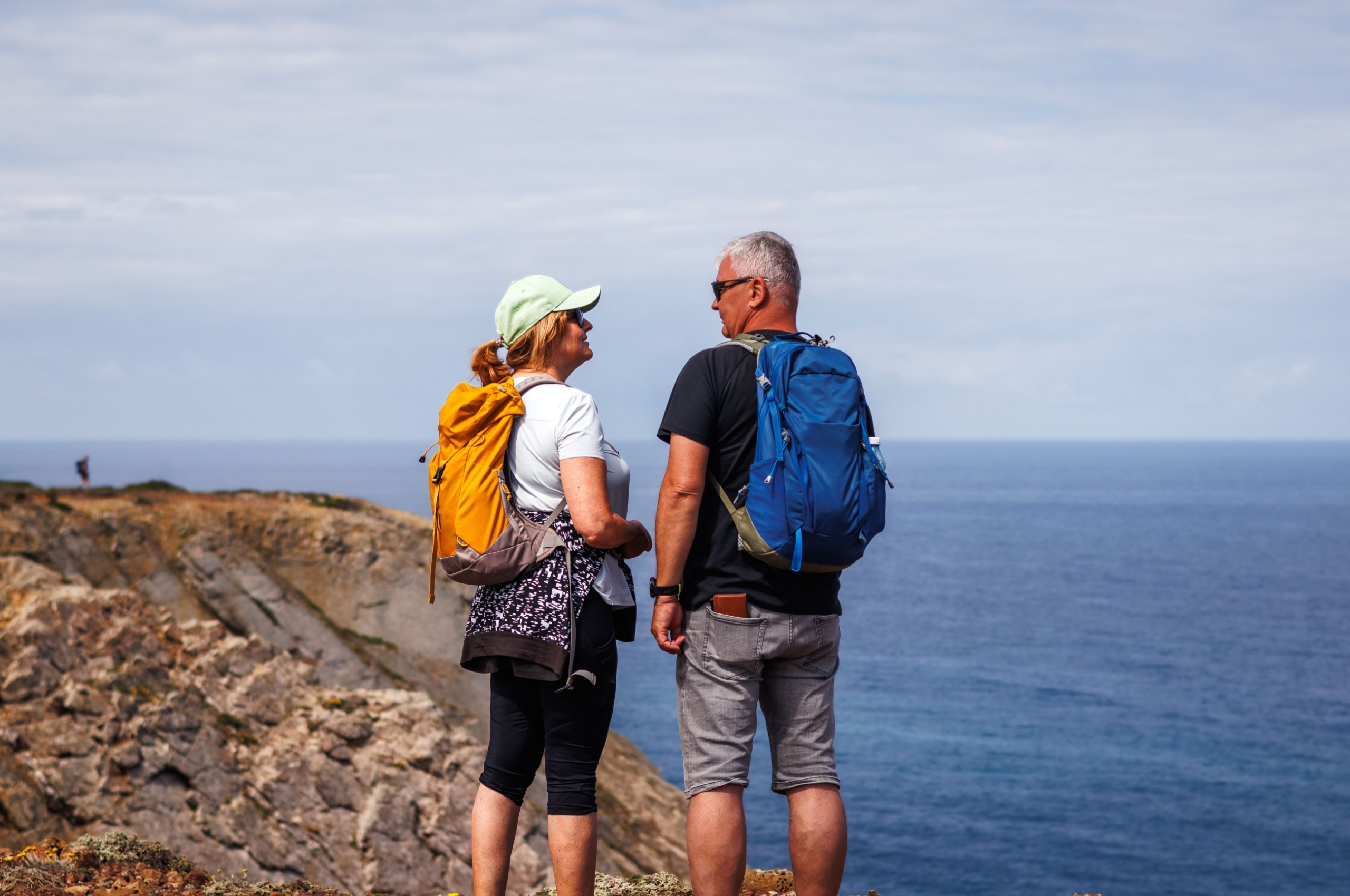 Middle-aged hiker couple stands on a rocky clifftop by the sea