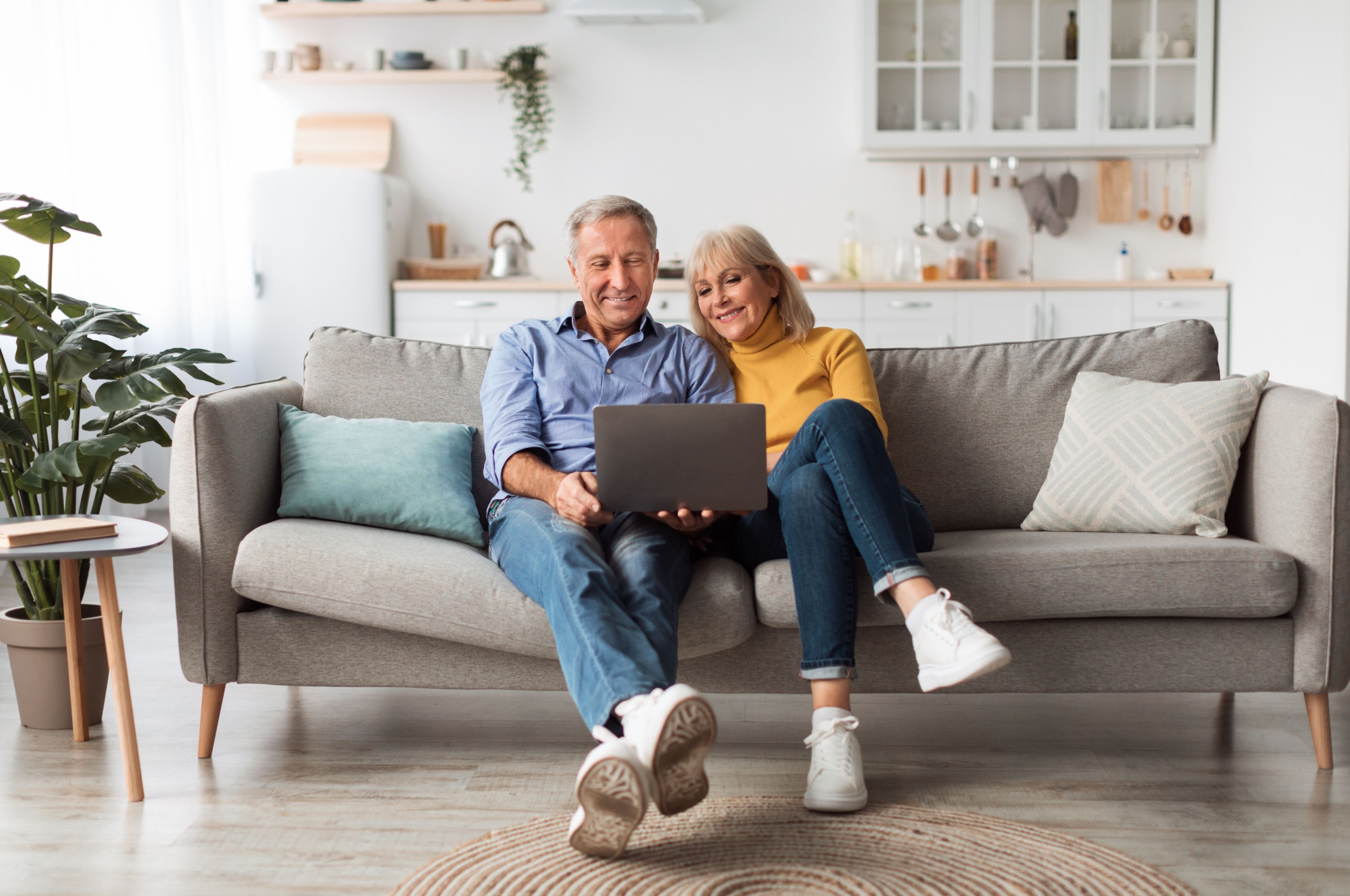 Smiling middle-aged couple look at laptop while sat on a sofa