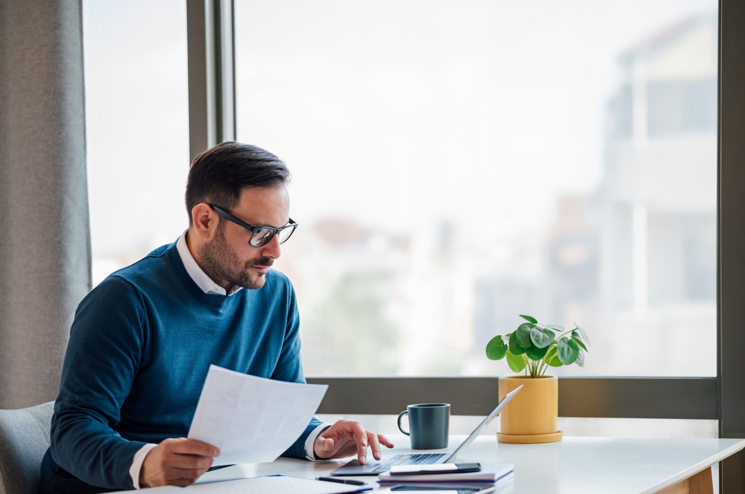 Business owner looking at a sheet of paper and using laptop